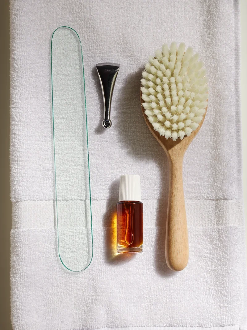Glasfeile, Nagelhautschieber, Nagelbürste und Nagelöl auf einem sauberen weissen Handtuch